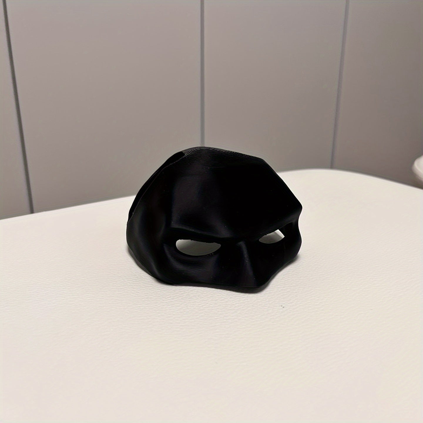 Black mask on a white surface with a gray tiled wall background