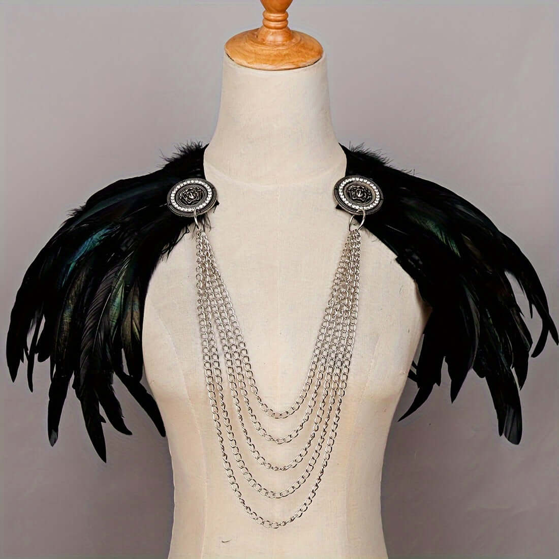 Feathered shoulder piece with chains on a mannequin against a gray background