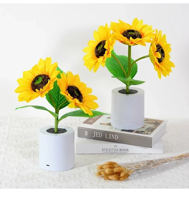 Two small potted sunflowers on a textured surface with books underneath.