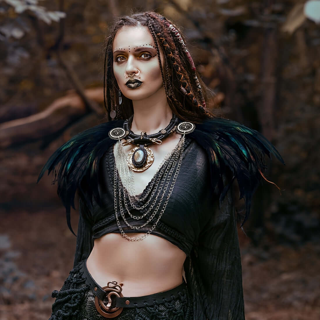 Woman in dark, elaborate costume with feathered shoulders against a natural background